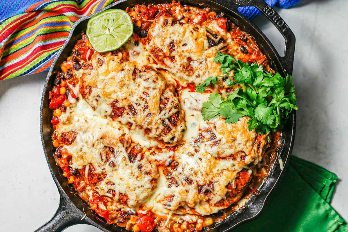 A cast iron skillet with cowboy chicken topped with melted cheese with sprigs of cilantro to the side.