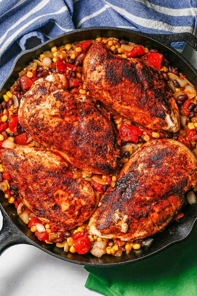 Seared chicken breasts nestled in a mixture of beans, tomatoes and corn in a cast iron skillet.