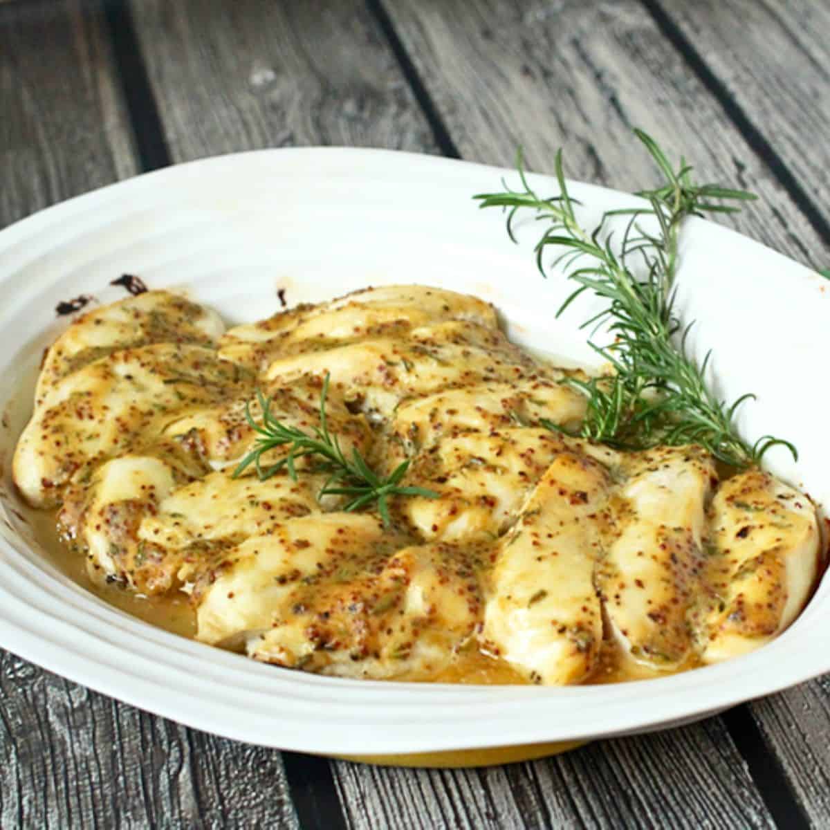 A white oval serving platter with honey Dijon chicken strips after baking and rosemary sprigs to the side for garnish.