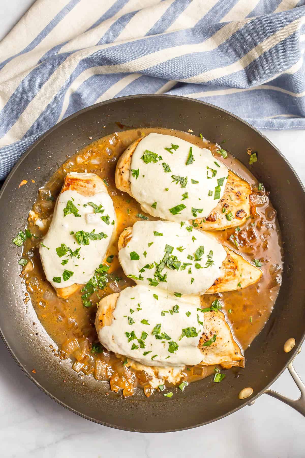 Four chicken breasts in a dark skillet with melted mozzarella cheese and parsley.