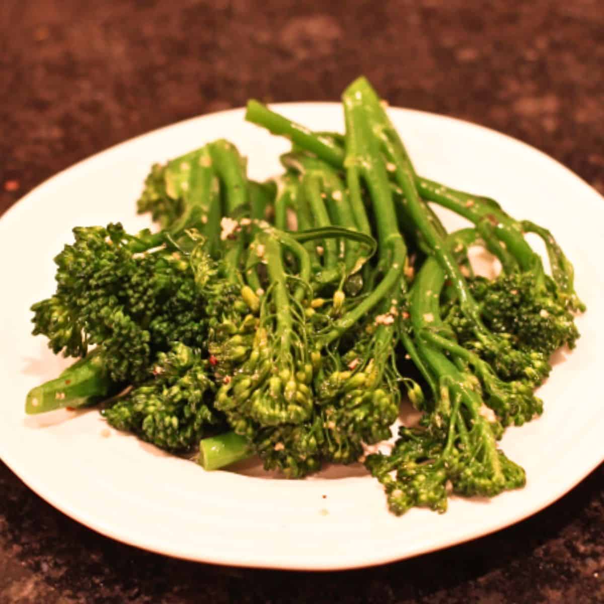 A low white bowl filled with long stalks of garlicky broccolini.