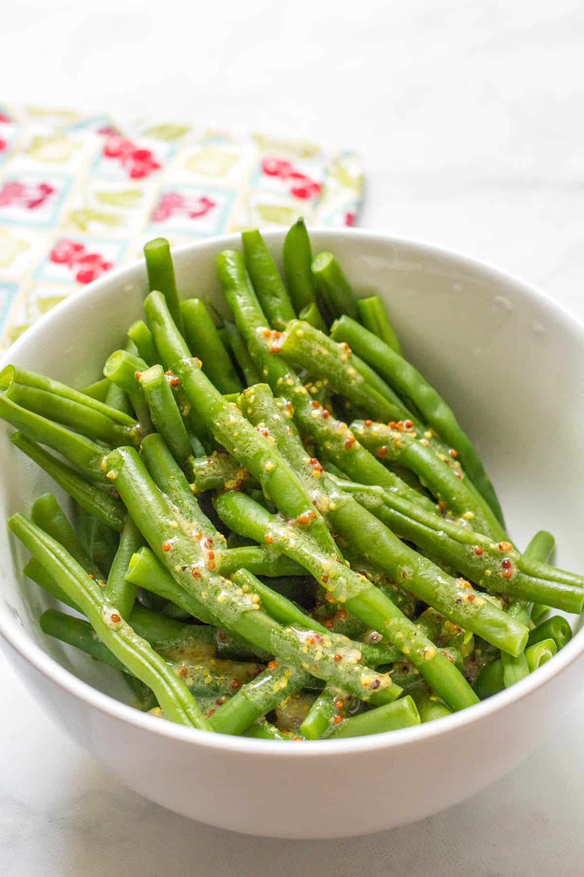 Steamed green beans with mustard butter sauce drizzled over top in a white bowl.