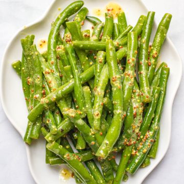 Close up of green beans with mustard butter sauce on a white platter.