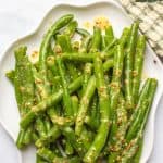 Green beans with mustard butter sauce served on a white platter with a text overlay on the photo.