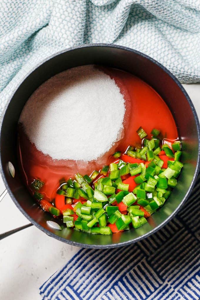 A medium saucepan with chopped peppers, sugar and a vinegar mixture before being stirred together.