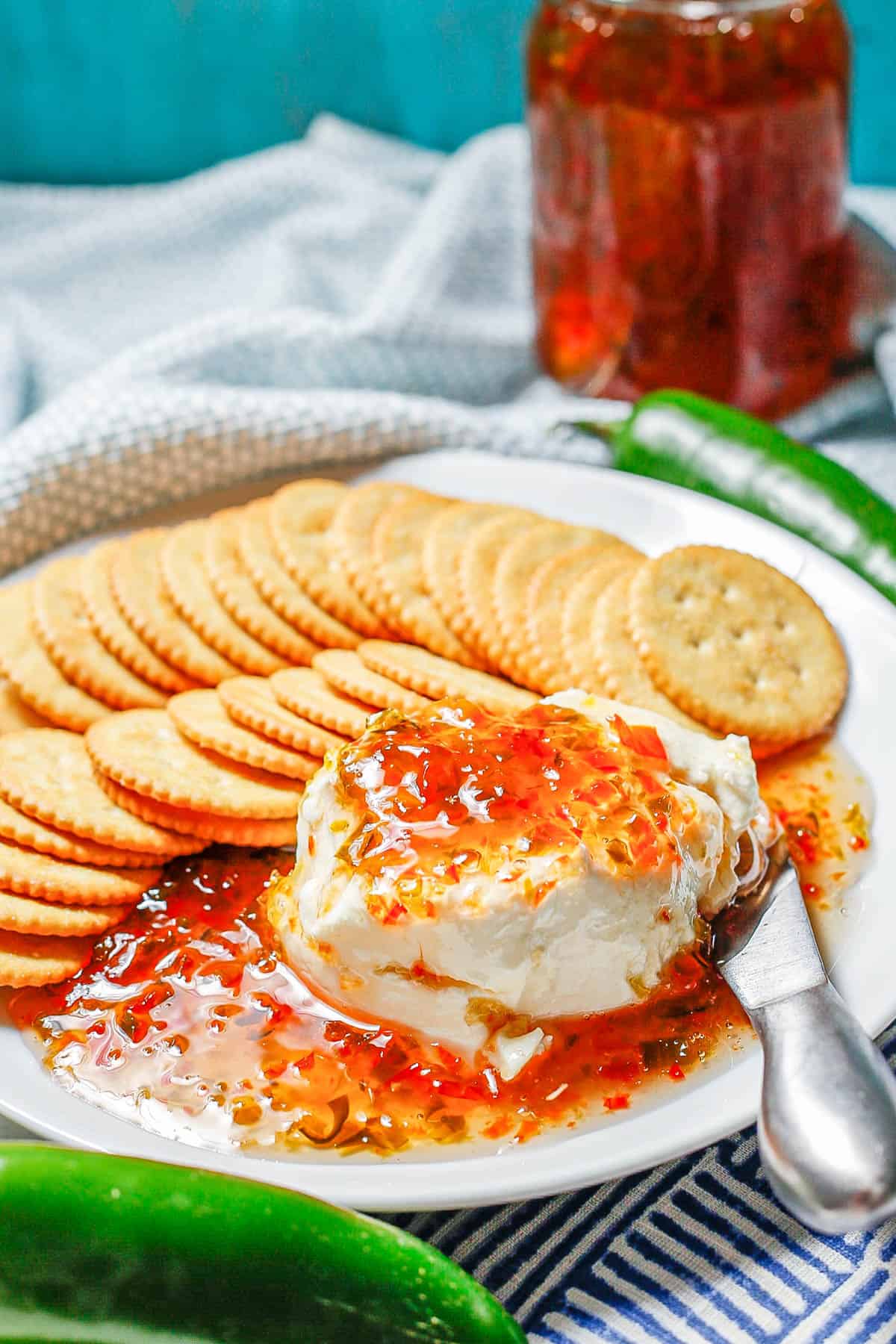 Cream cheese and pepper jelly served on a white round plate with crackers.