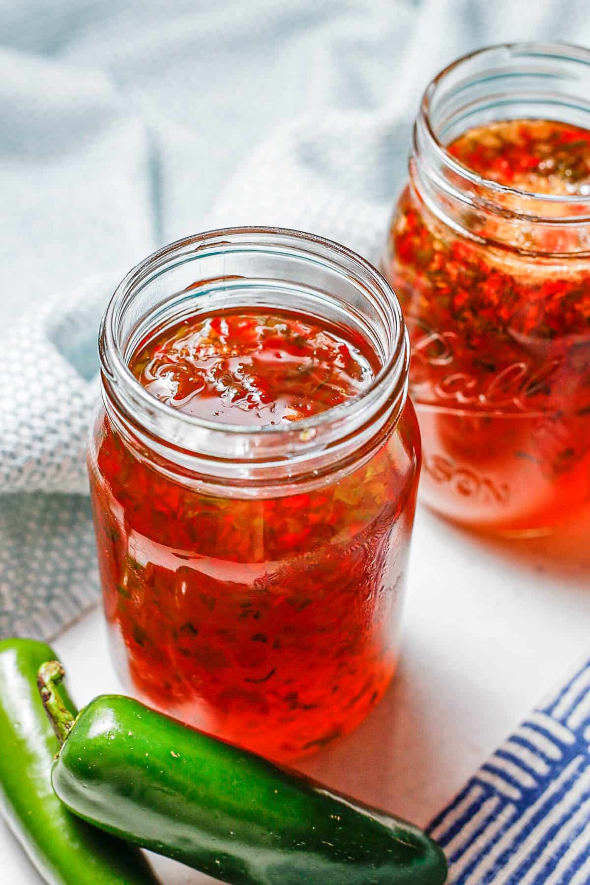 An open jar of pepper jelly alongside a couple of jalapeno peppers.