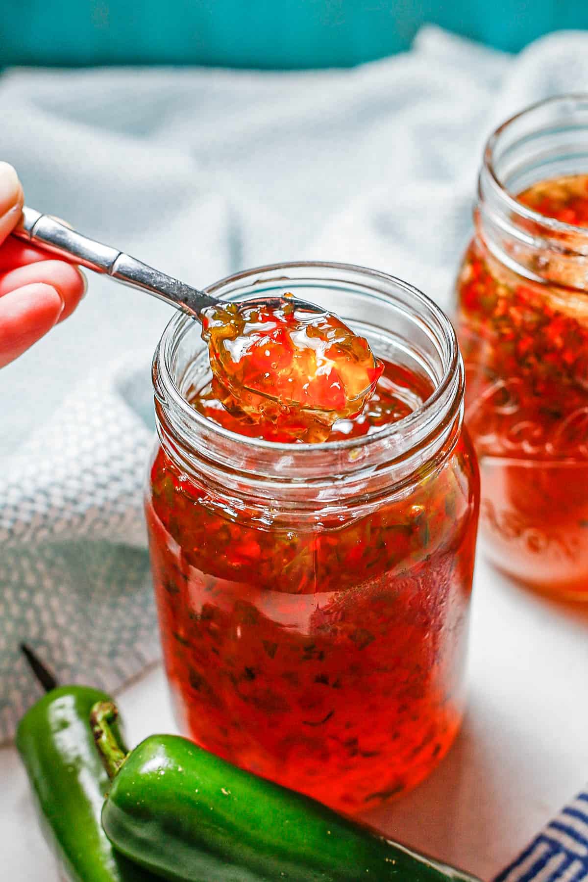 A spoon lifting up some pepper jelly from a glass jar.