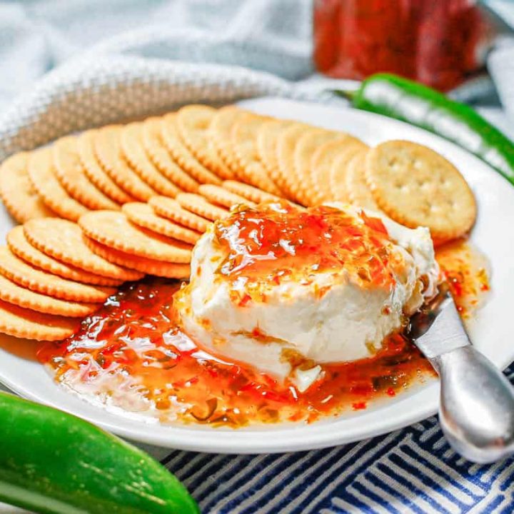 A white plate with cream cheese topped with pepper jelly and surrounded with crackers.