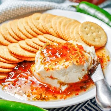 Close up of cream cheese and pepper jelly served on a white round plate with crackers.