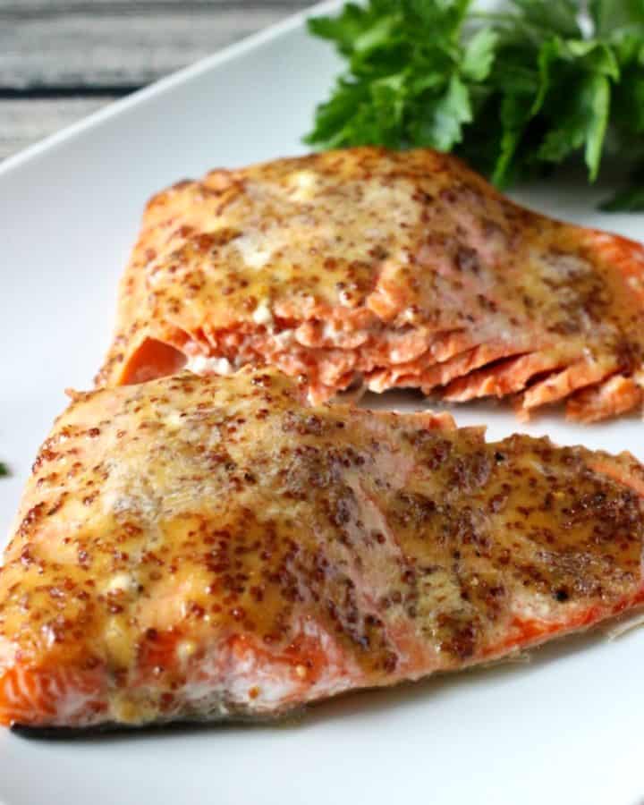 Two filets of wild salmon topped with a honey Dijon mixture and served on a rectangular white plate with parsley to the side as garnish.