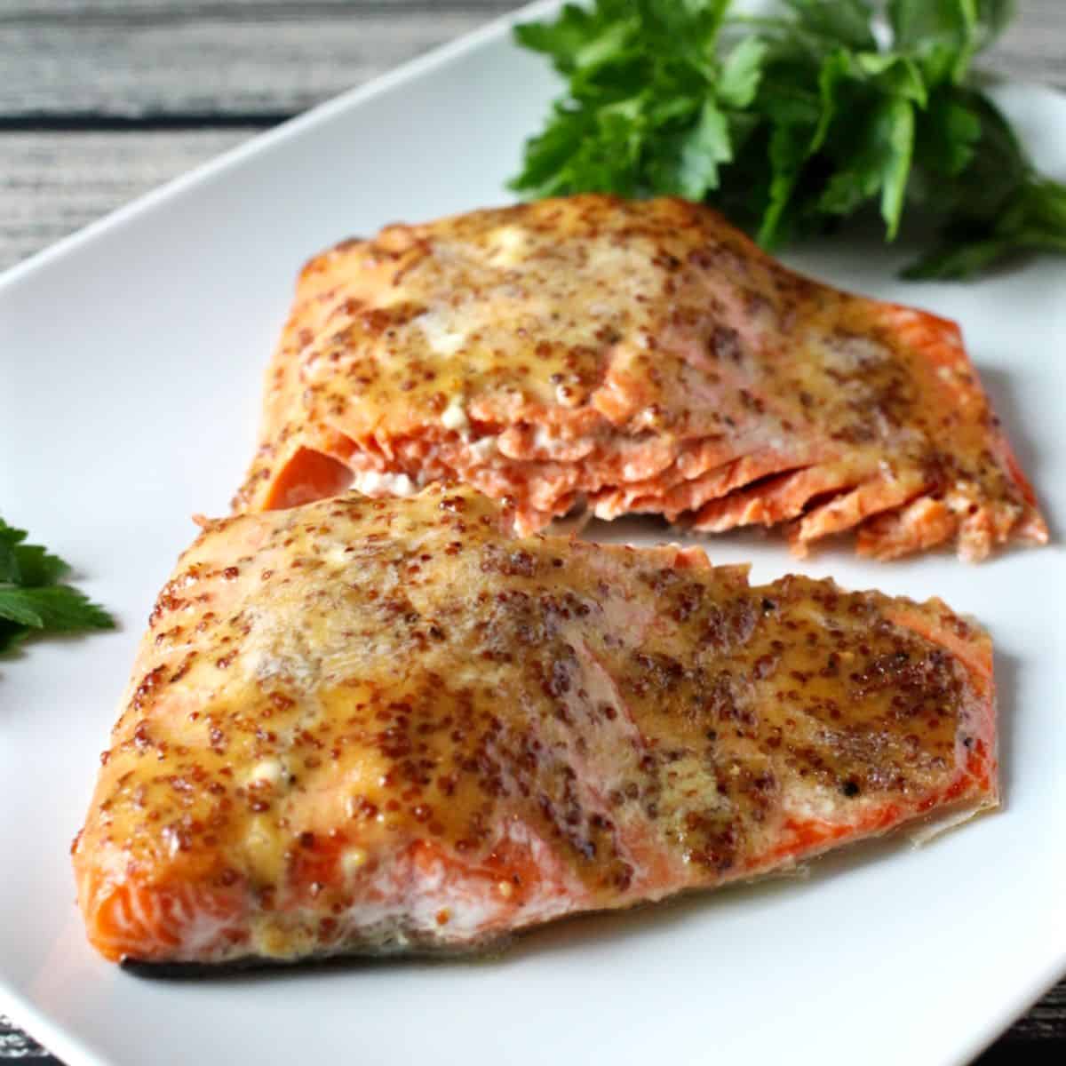 Two filets of wild salmon topped with a honey Dijon mixture and served on a rectangular white plate with parsley to the side as garnish.