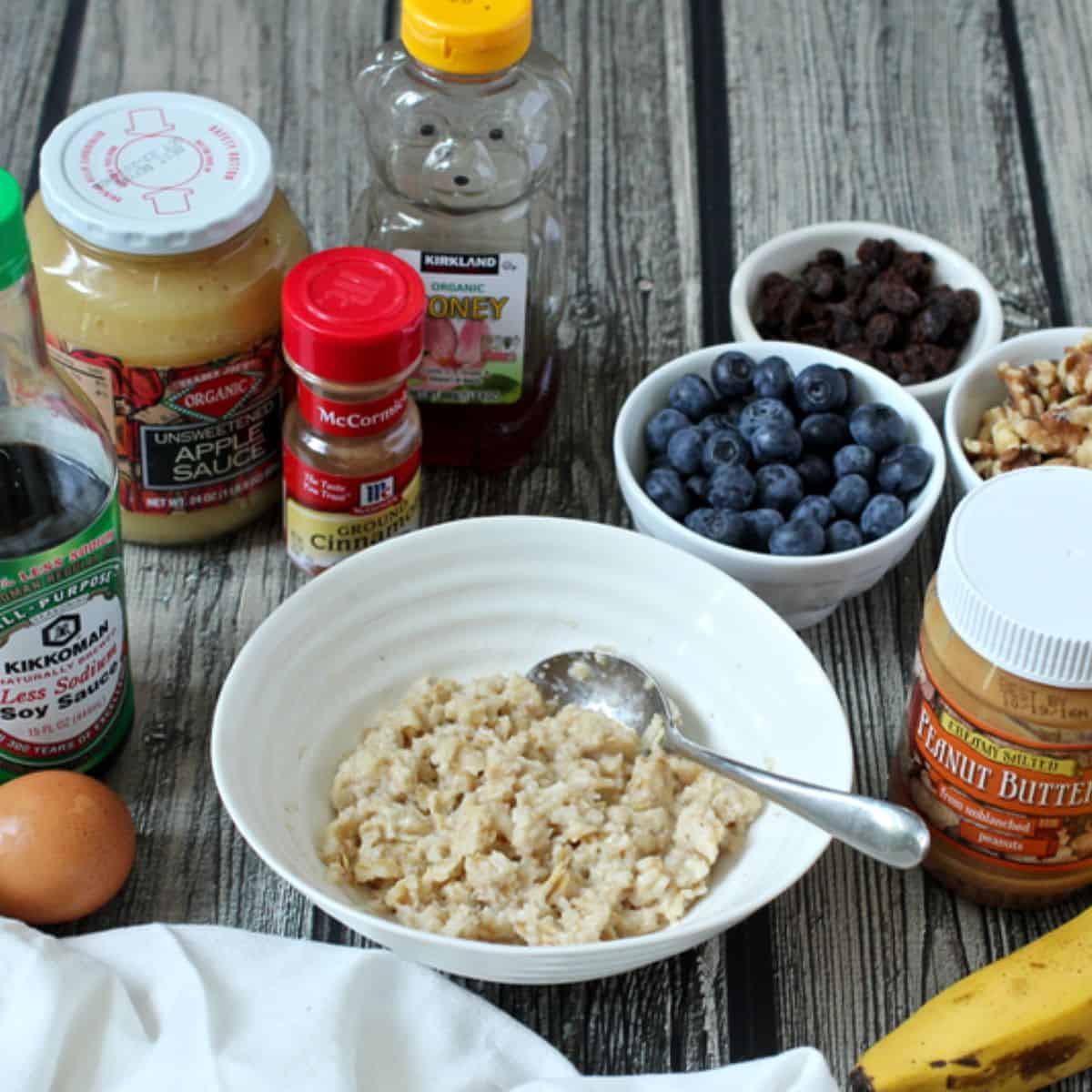 A bowl of oatmeal with a spoon resting in it and a variety of topping options laid out around the bowl.