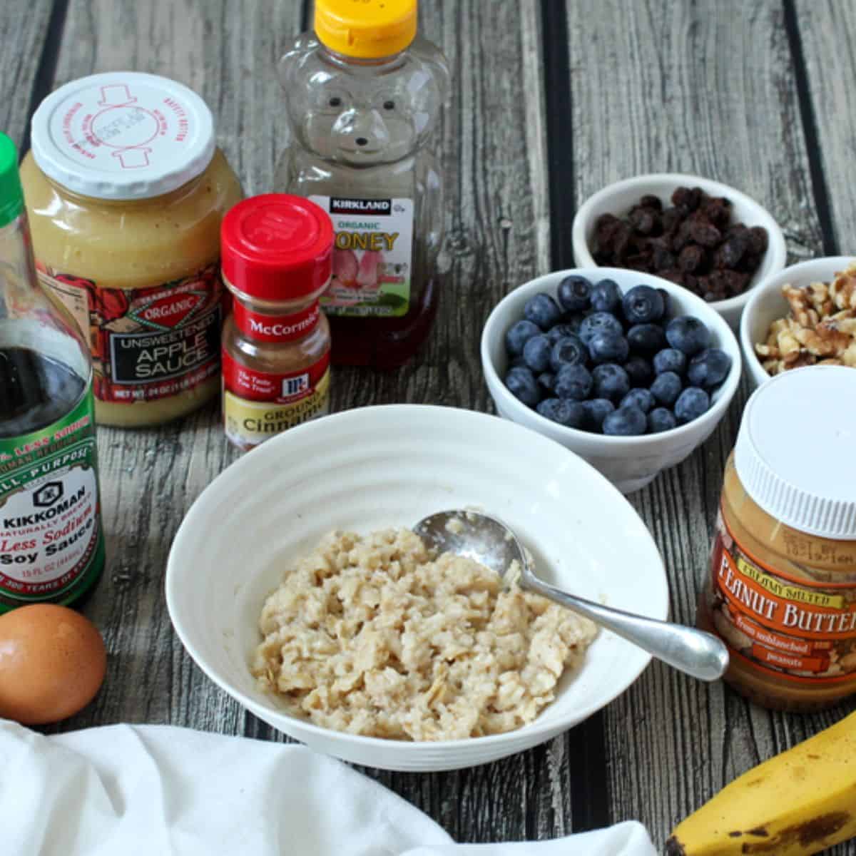 A bowl of oatmeal with a spoon resting in it and a variety of topping options laid out around the bowl.