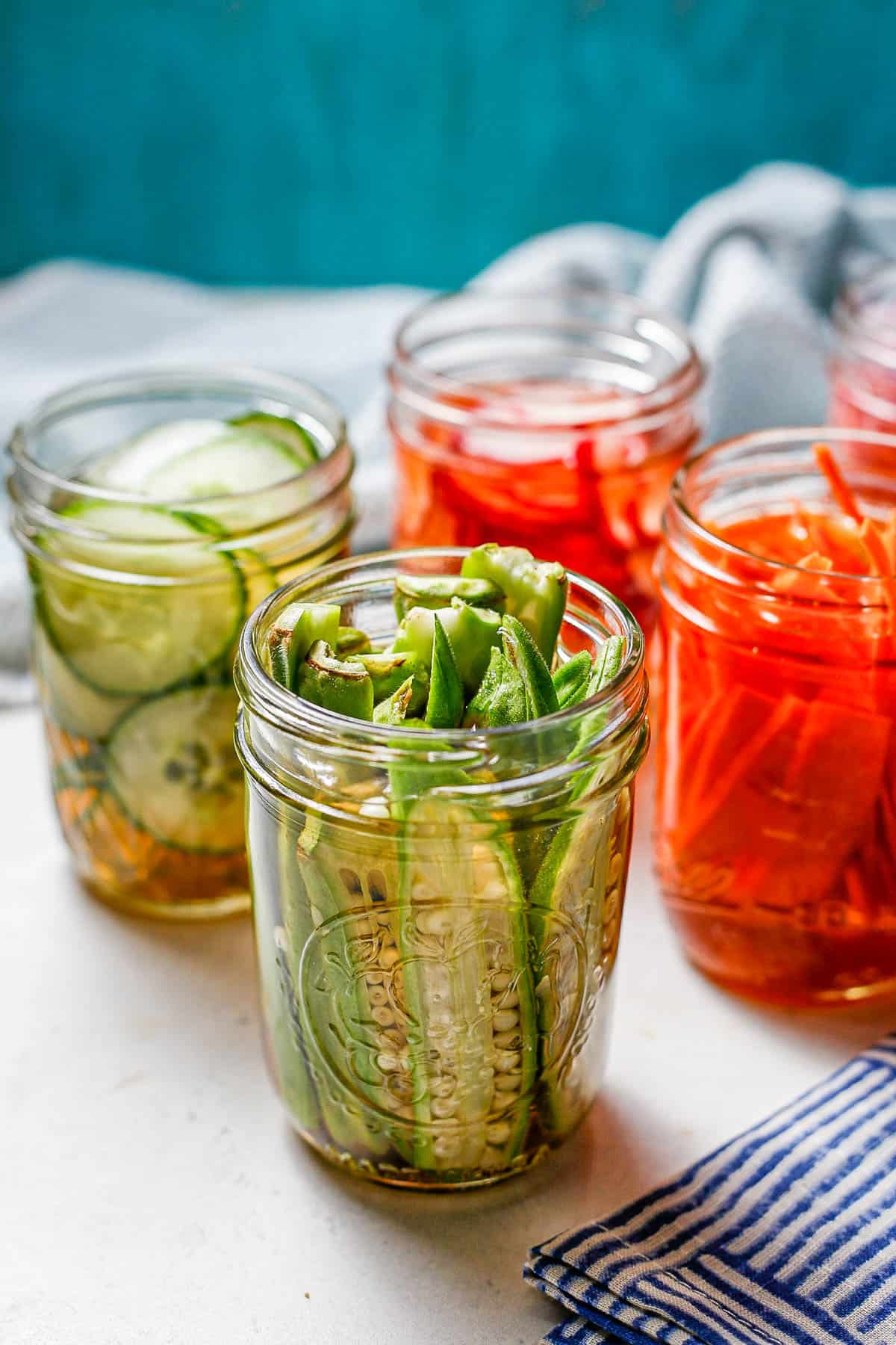 Pickled okra in a small glass jar with other pickled veggies in the background.