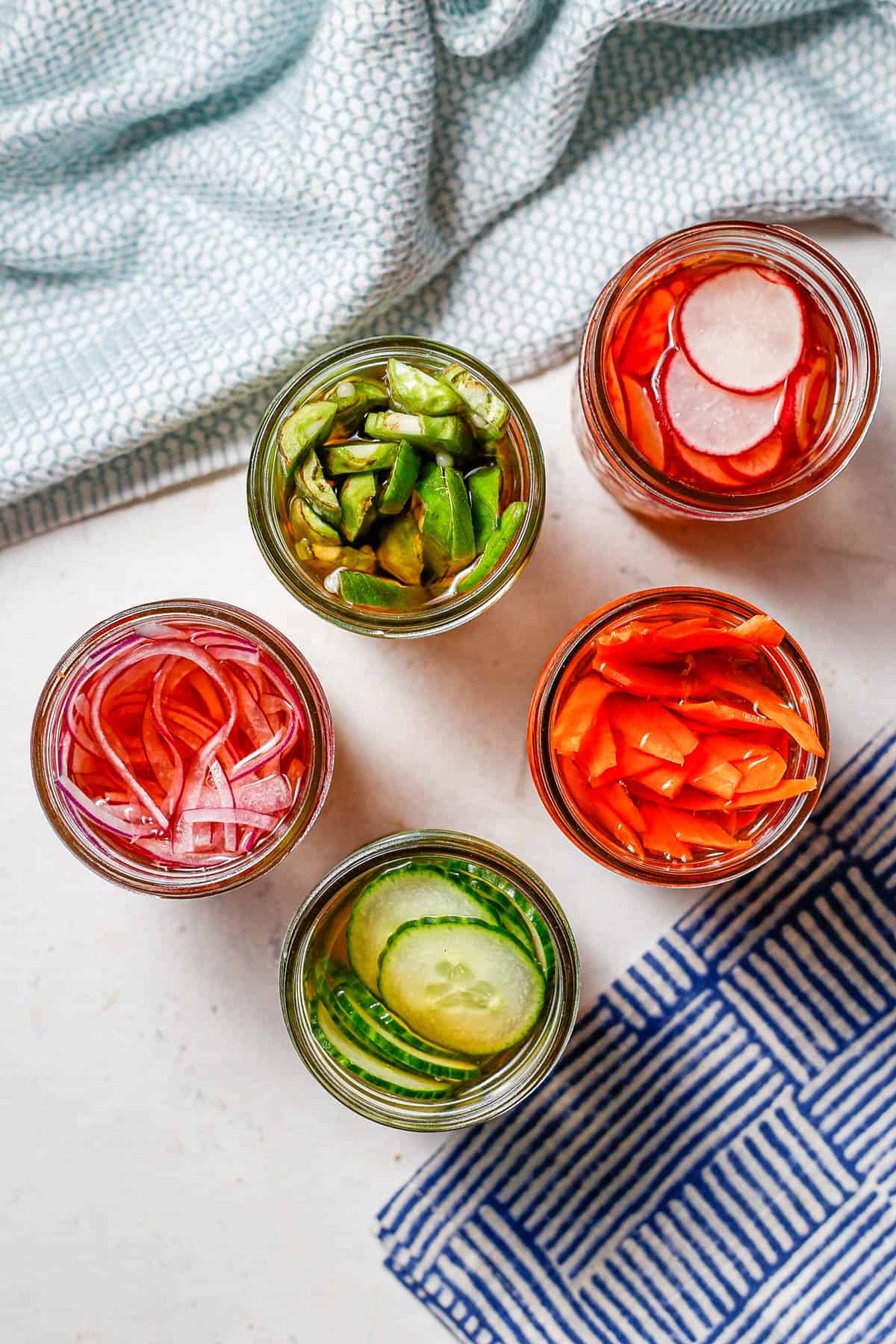 Overhead view of five small glass jars with different pickled vegetables in each one.