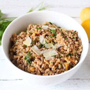 A white bowl with a farro salad with parsley, chopped nuts, red pepper flakes and Parmesan shavings on top.