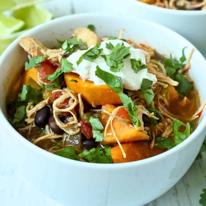 A small bowl of soup with shredded chicken, sweet potatoes, black beans, tomatoes and roasted poblano peppers.