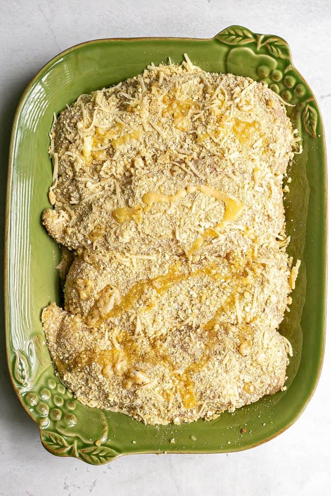 Breadcrumb and cheese coated chicken breasts in a baking dish before being baked.