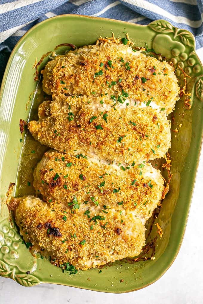 Crispy browned baked cheesy chicken breasts in a green casserole dish with parsley sprinkled on top.