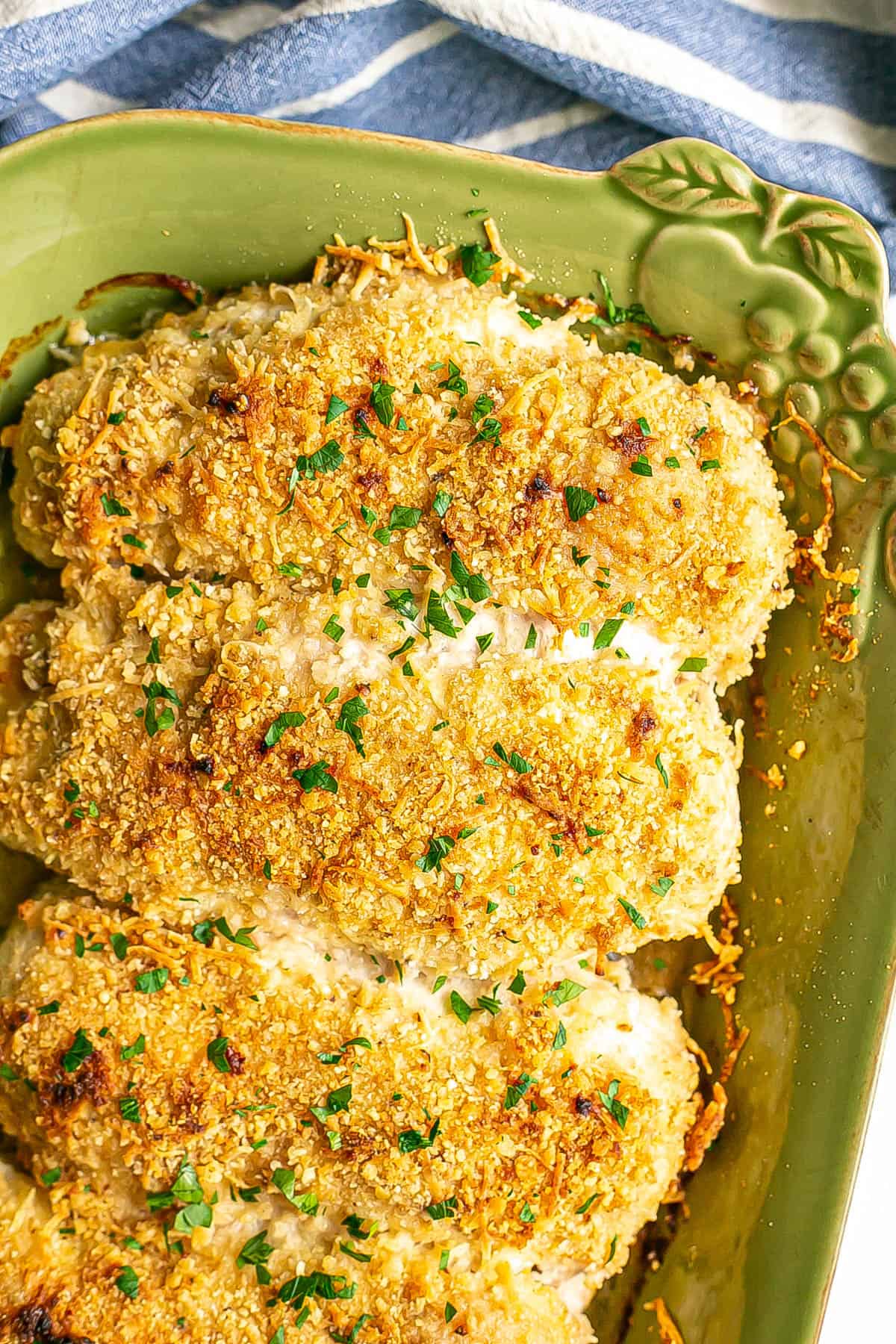 Crispy browned baked cheesy chicken breasts in a green casserole dish.