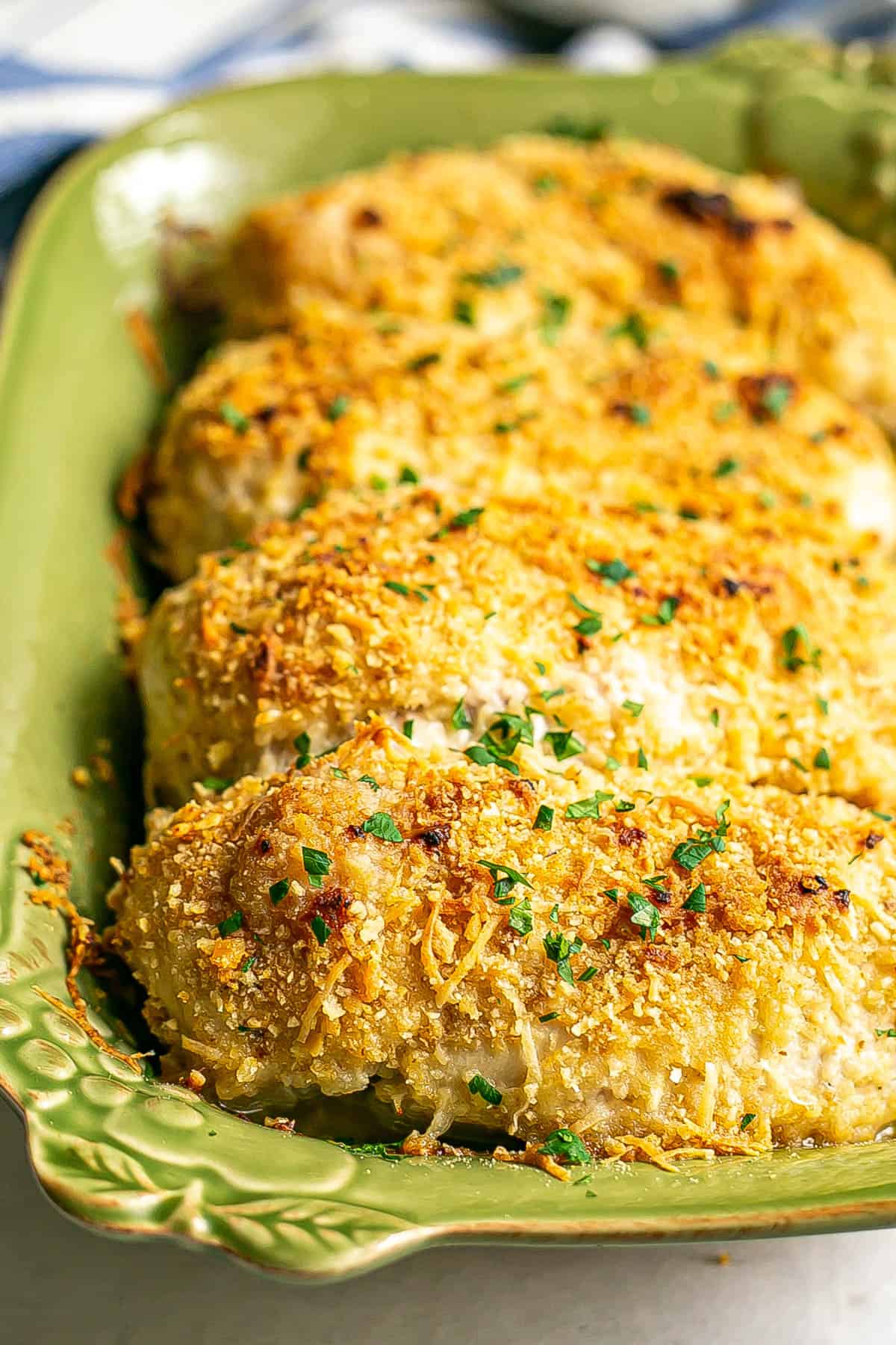 Close up of crispy browned cheesy baked chicken breasts in a green casserole dish.