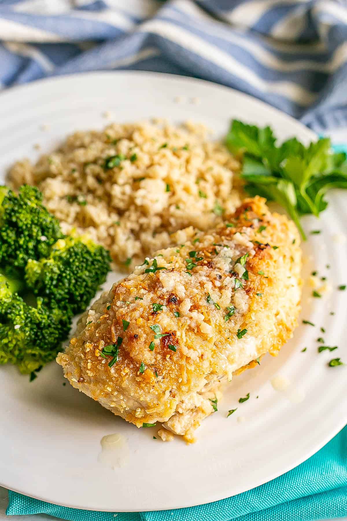 A cheesy chicken breast served on a white dinner plate with rice and broccoli.