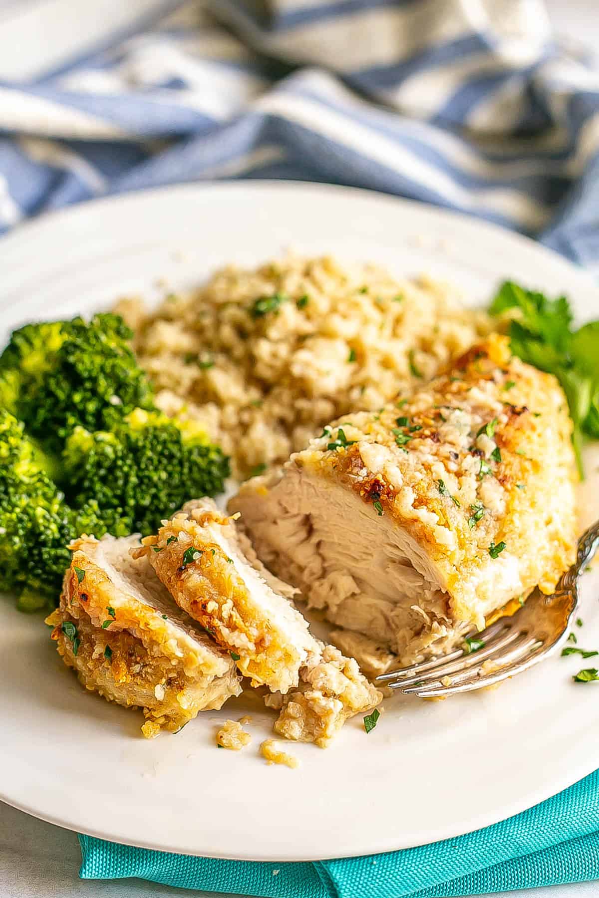A sliced, breaded cheesy chicken breast served on a white dinner plate with rice and broccoli.