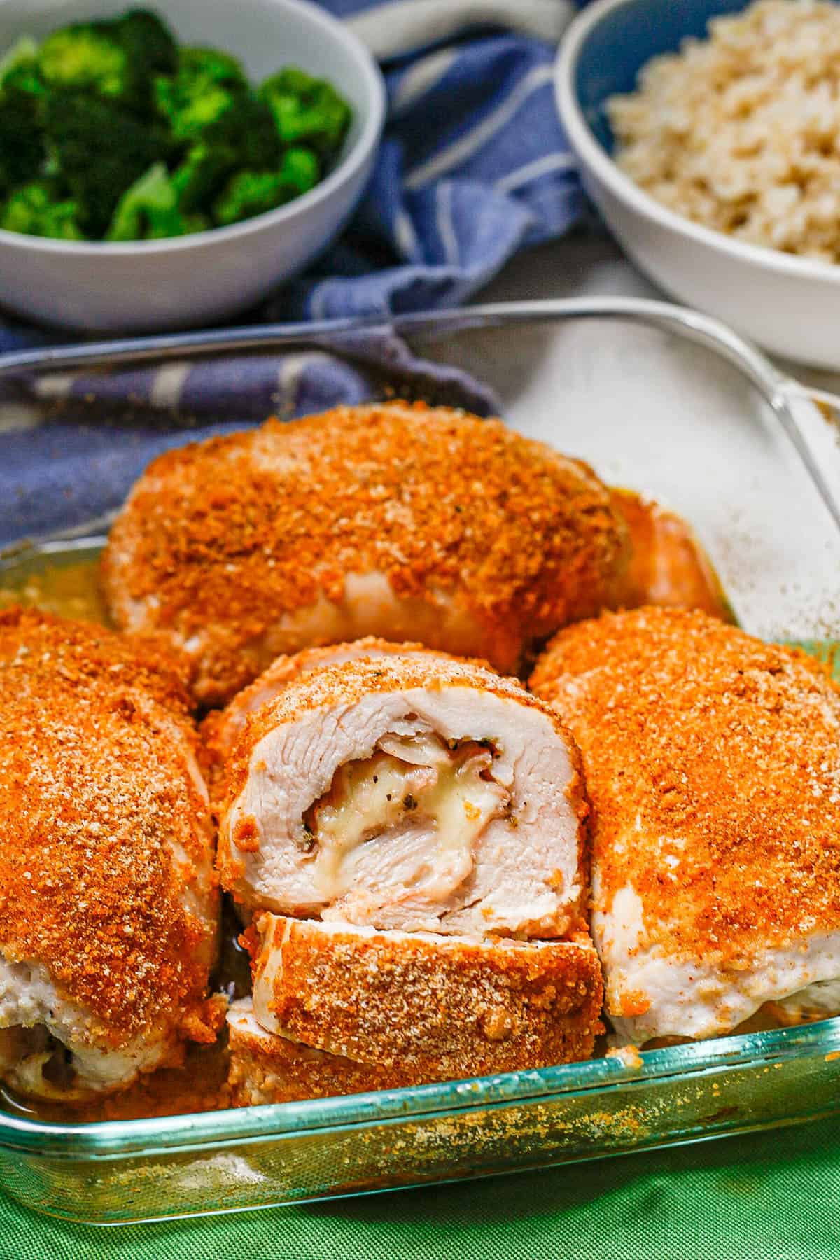 A glass casserole dish with baked chicken cordon bleu with one sliced to show the inside stuffing.