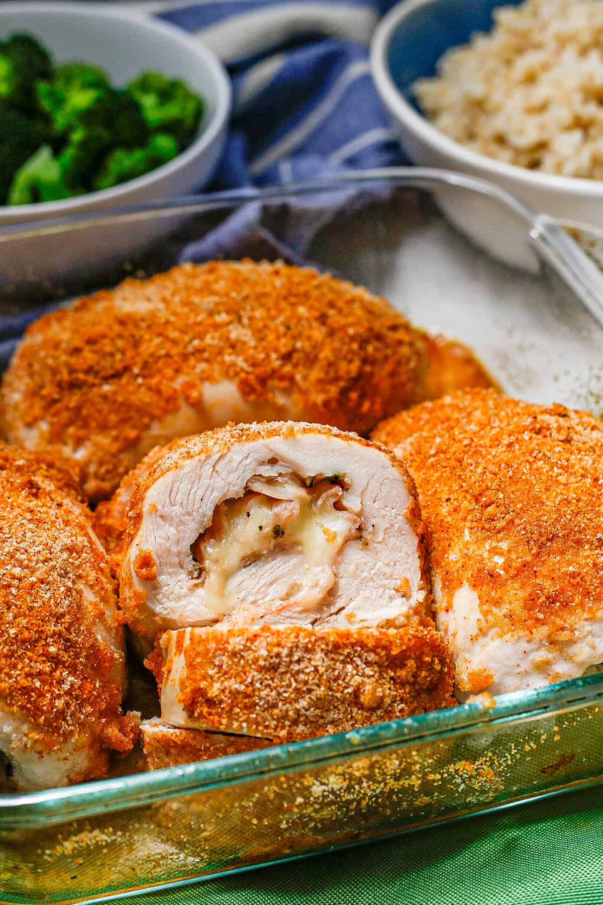 Close up of a glass casserole dish with baked chicken cordon bleu with one sliced to show the inside stuffing.