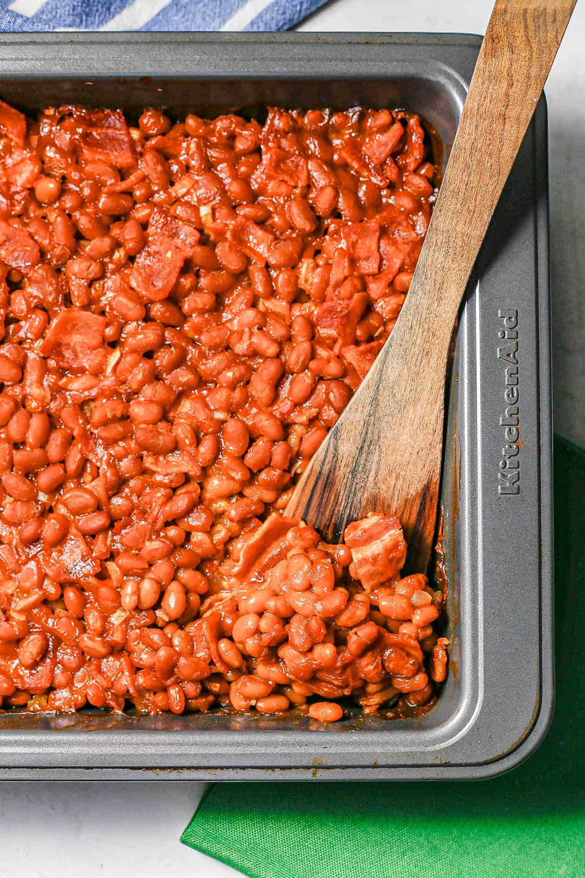 A wooden spatula resting in a pan of baked beans with bacon.