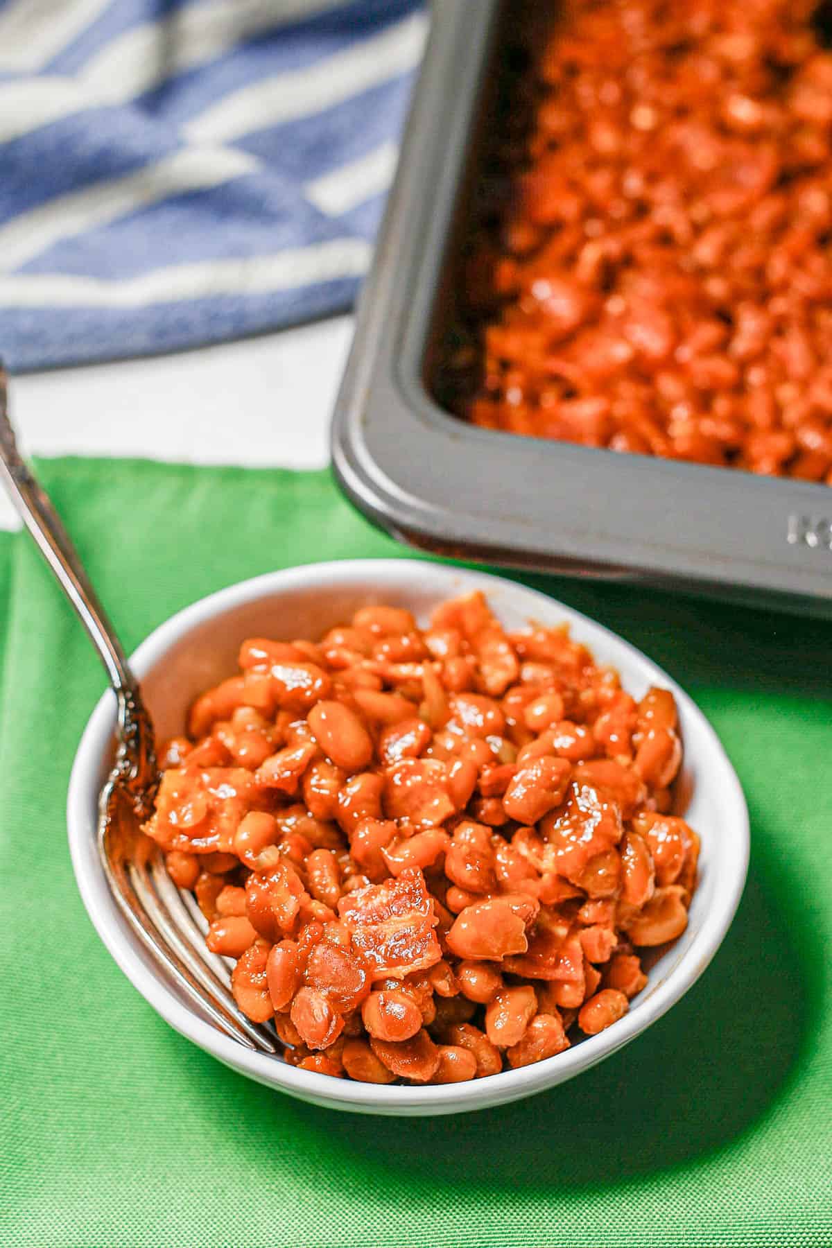 A small white bowl set on green napkins with a serving of baked beans.