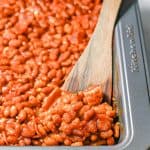 A wooden spatula resting in a pan of baked beans and a text overlay on the photo.