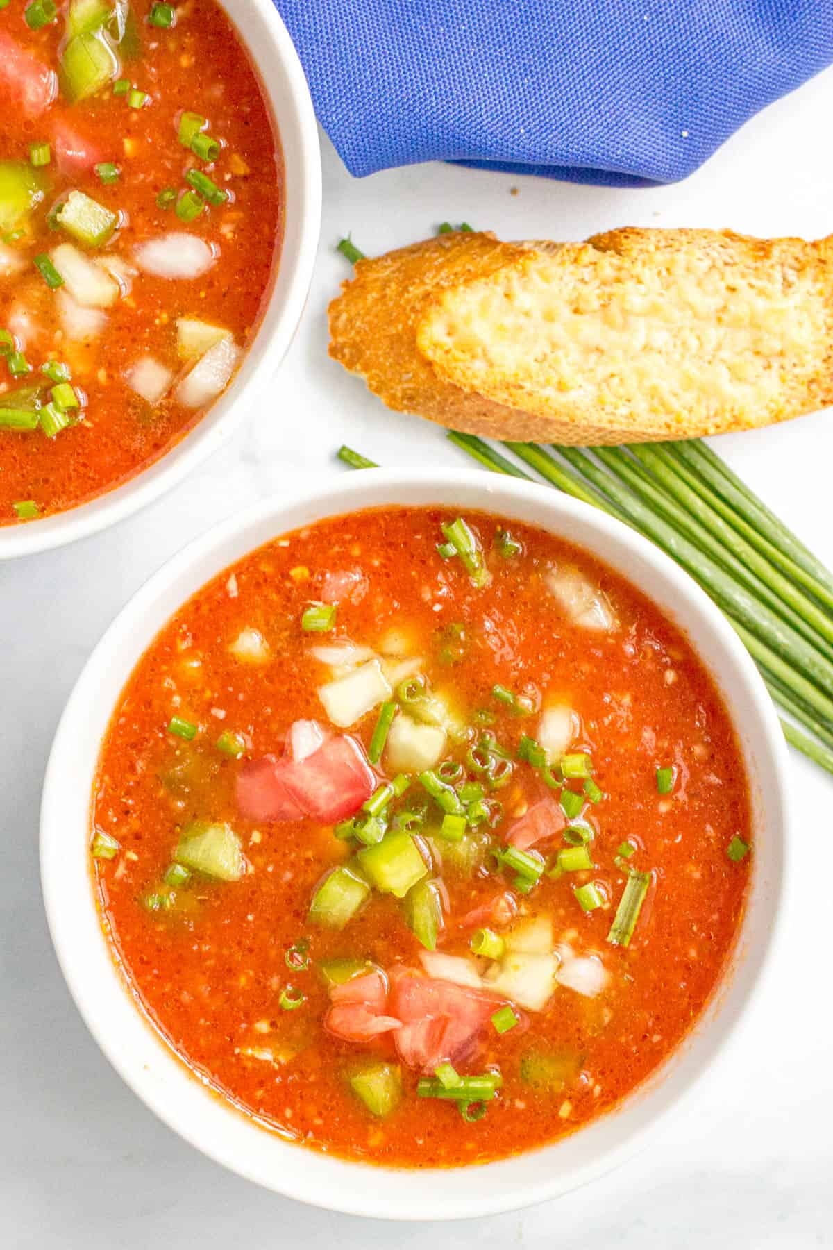 Close up of white bowls of gazpacho soup with bread to the side.