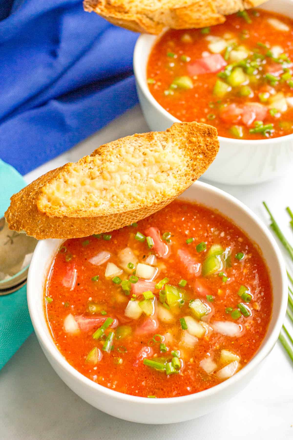 Two bowls of gazpacho with a piece of cheesy baguette slices resting on the side of the bowls.