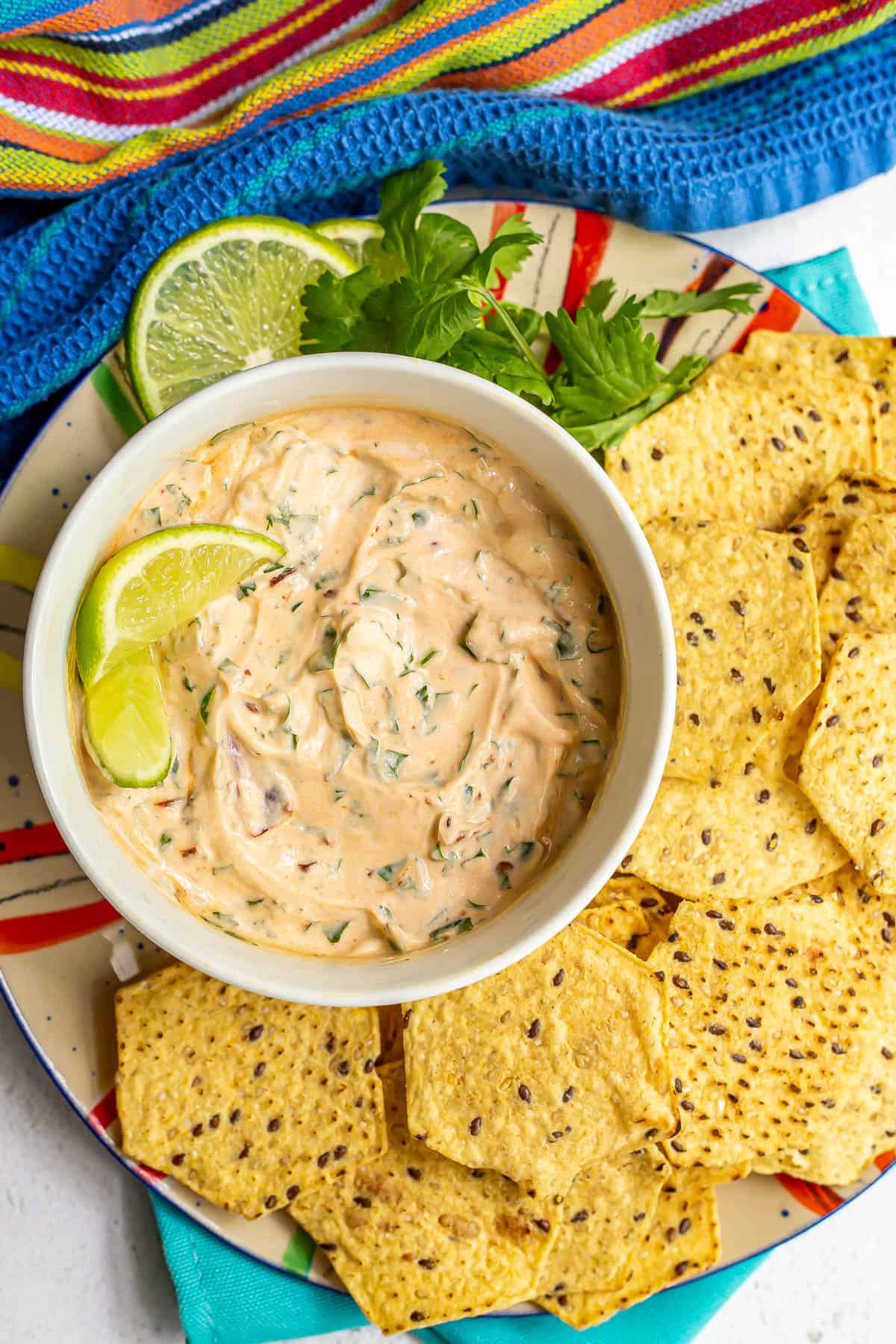 A creamy chili Greek yogurt dip served in a bowl with a garnish of lime wedges and tortilla chips served for dipping.