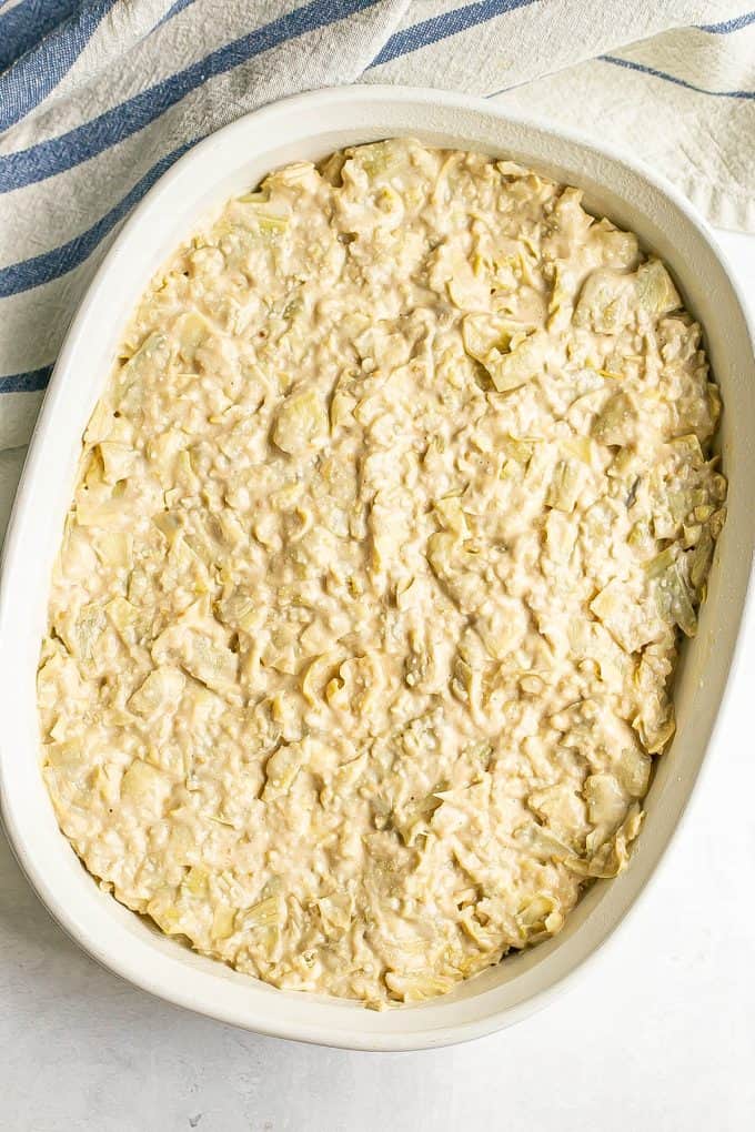 Creamy artichoke dip spread in an oval casserole dish before being baked.