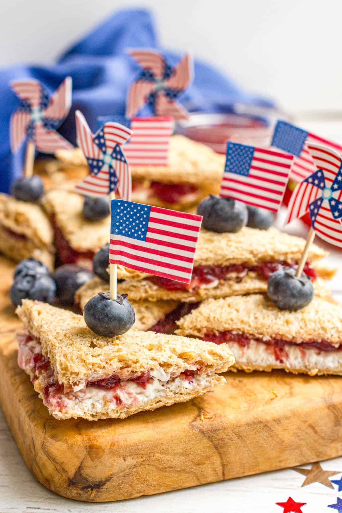 Mini triangle sandwiches with cream cheese, strawberry jam and a blueberry on top held in place with mini American flags.