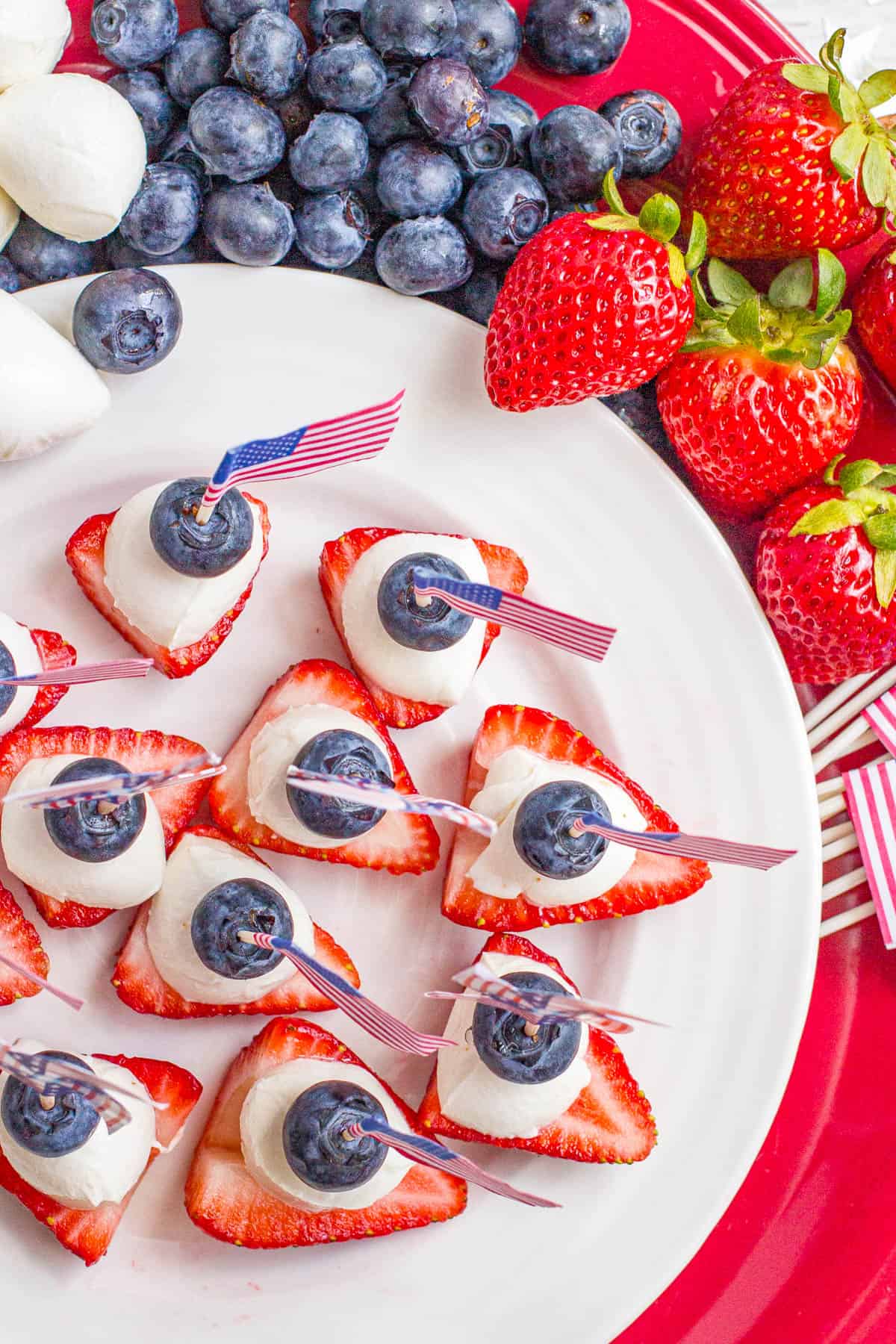 Red white and blue fruit and mozzarella stacks served on a white plate with extra fruit and cheese to the side.