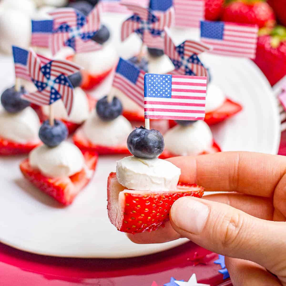 A hand holding up a half of a hulled strawberry stuffed with a mozzarella ball and blueberry for a red white and blue snack.