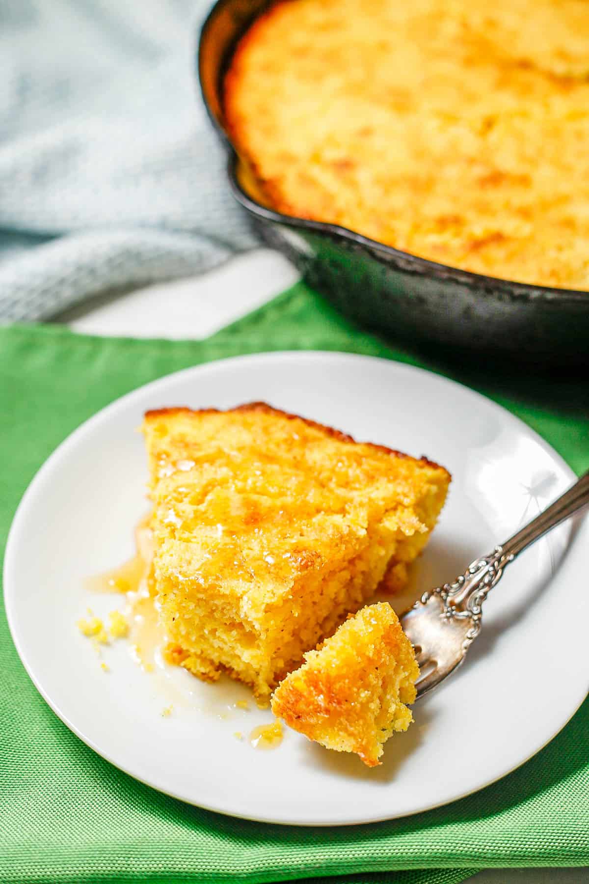 A fork resting on a white plate with a piece of cornbread taking from a slice.