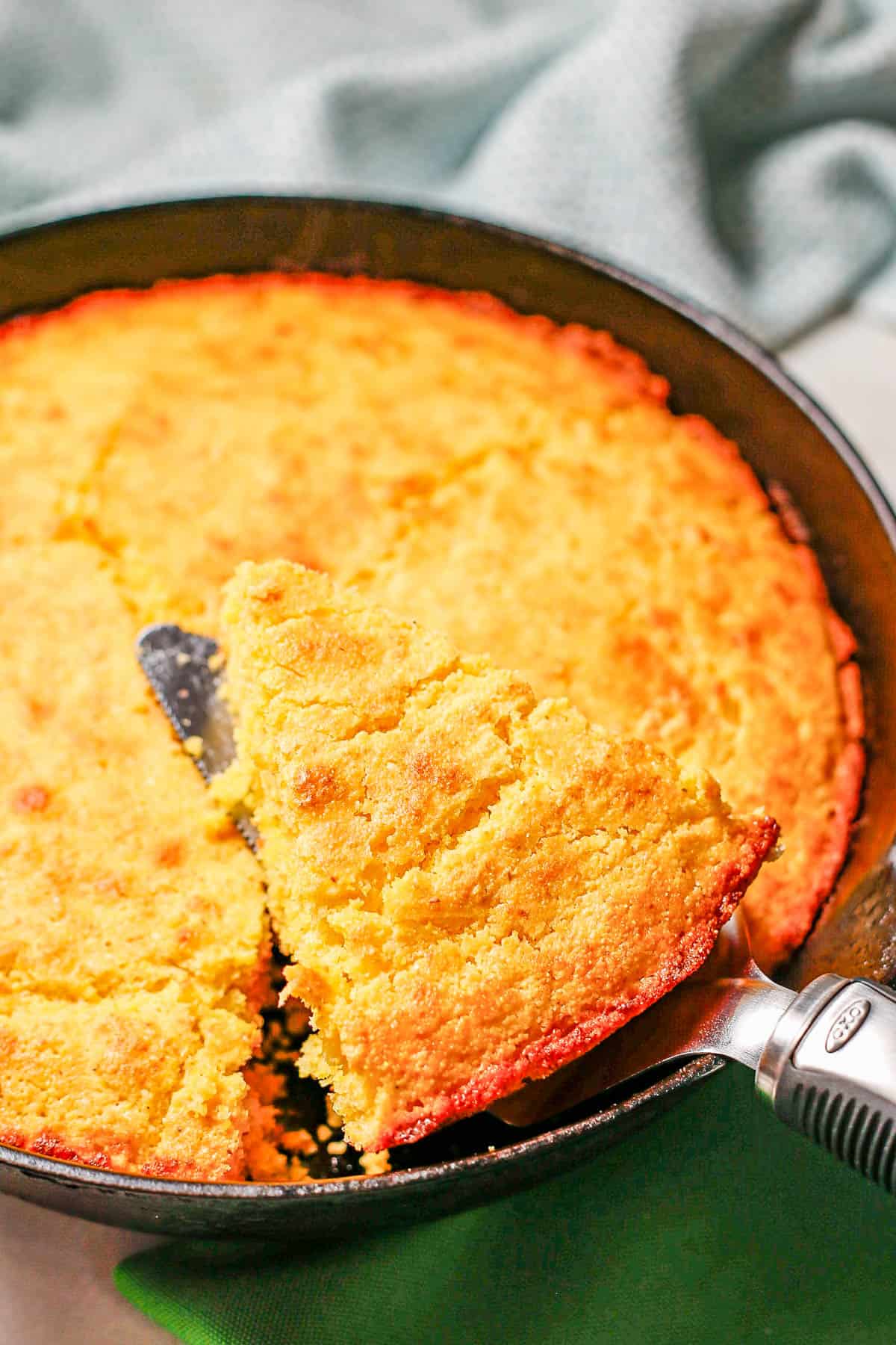 A pie server lifting up a slice of cornbread from a cast iron skillet.