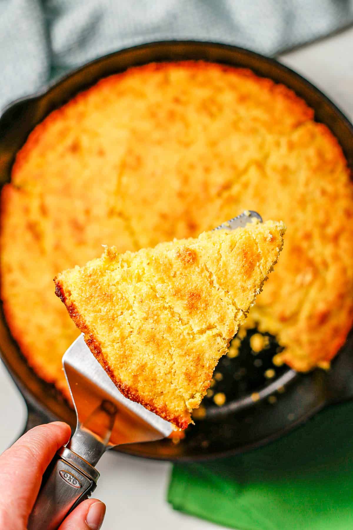 A pie server holding up a slice of cornbread above a cast iron skillet.