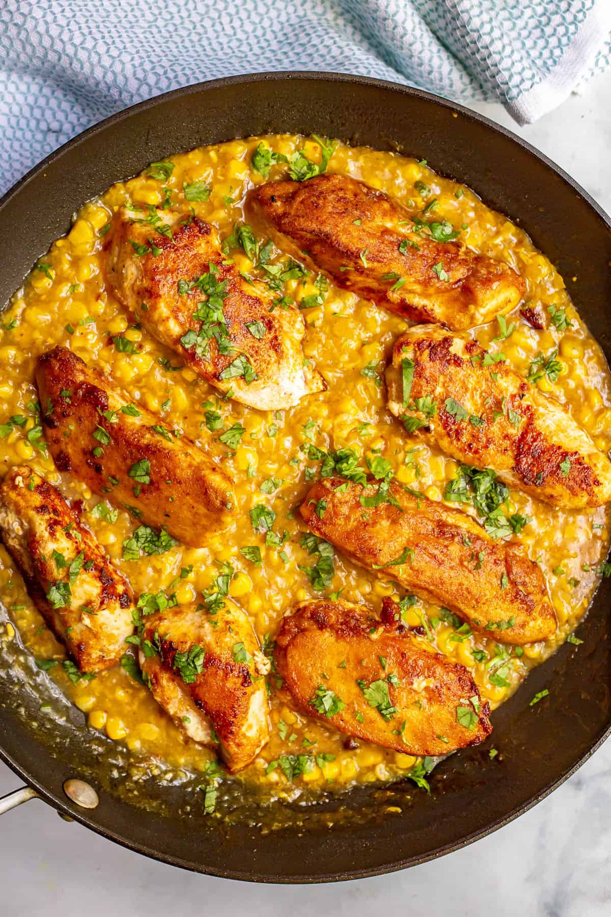 Skillet chicken with creamed corn in a large skillet with cilantro sprinkled on top.