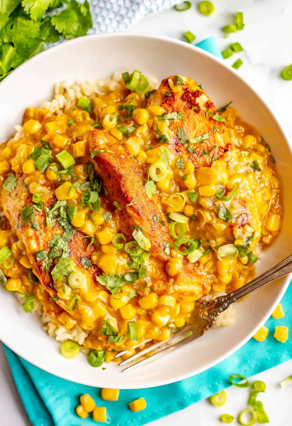 A low white bowl with seared skillet chicken with creamed corn, topped with cilantro and green onions and a fork resting in the bowl.