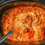 A scoop of slow cooker BBQ chicken being lifted out of the crock pot insert with a text overlay on the photo.