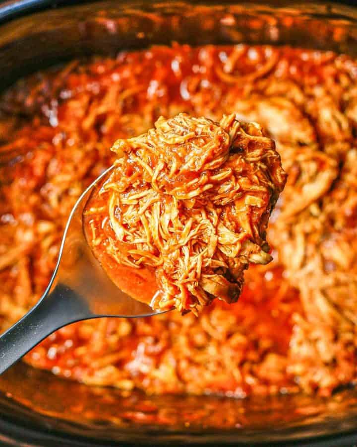 Close up of a scoop of slow cooker BBQ chicken being lifted out of the crock pot insert.