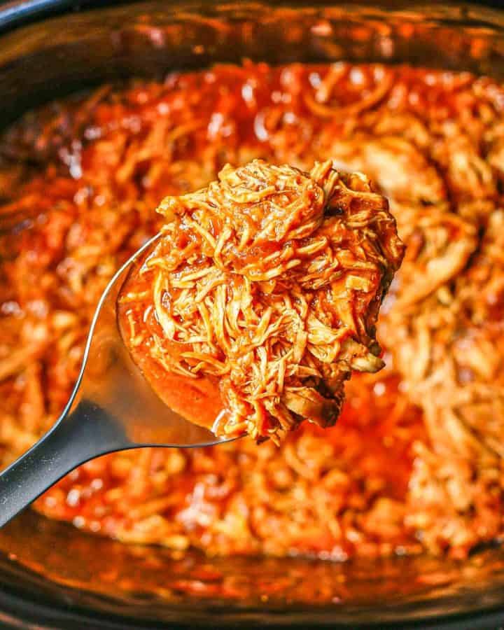 Close up of a scoop of slow cooker BBQ chicken being lifted out of the crock pot insert.