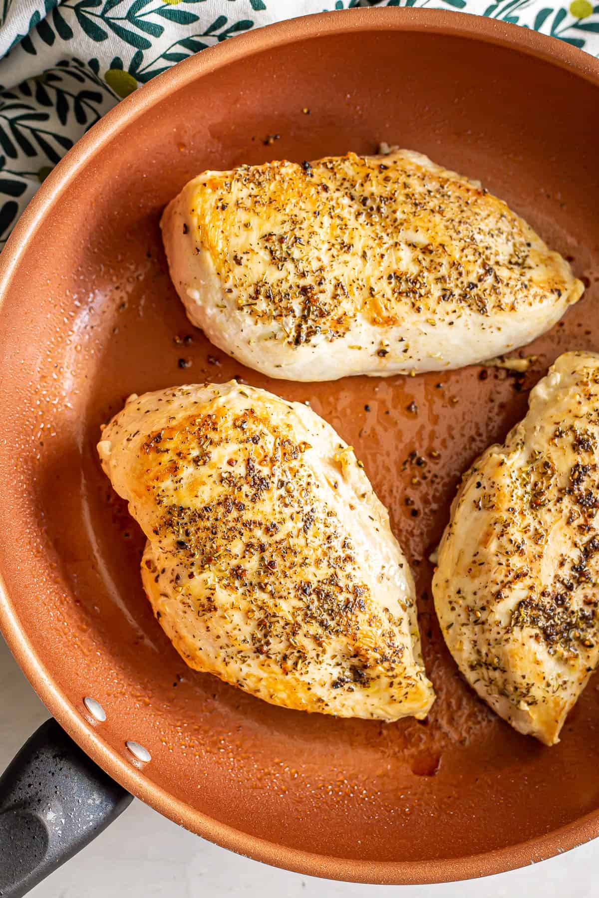 Three seasoned chicken breasts being seared in a copper skillet.