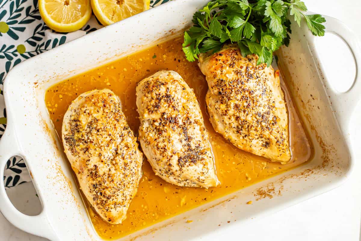 Three baked chicken breasts with garlic and lemon and sprigs of parsley to the side for garnish.